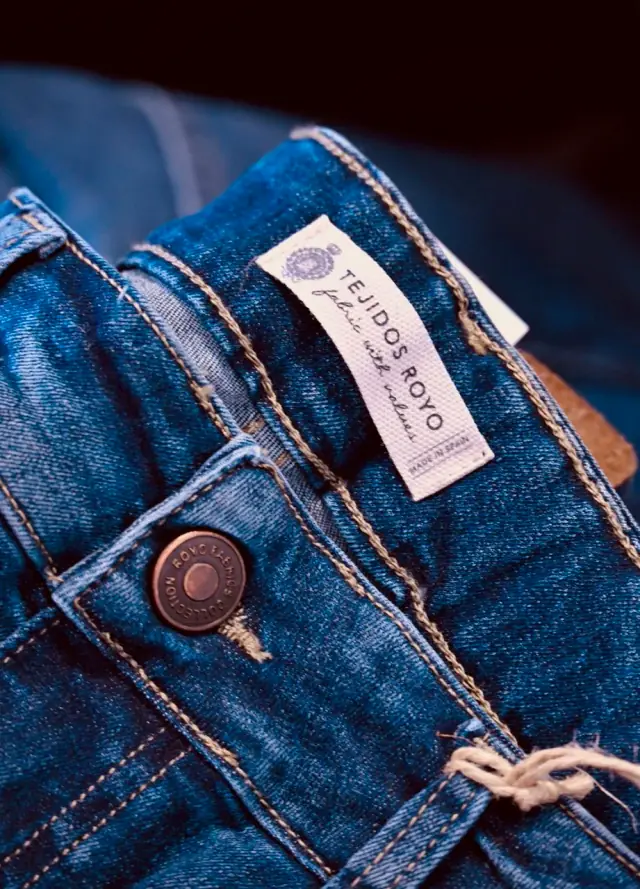 Detail of an indigo denim waistband with a copper branded shank button.